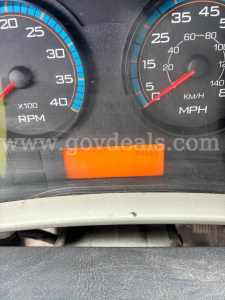Dashboard gauges from a dump truck showing tachometer and speedometer with an orange mileage display panel.