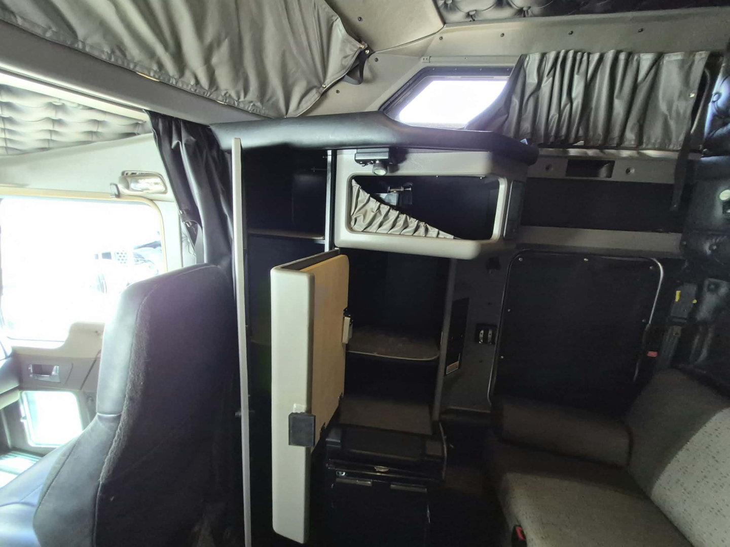 Kenworth W900L interior showing sleeper area with cabinets and overhead shelf in-service truck cabin view.