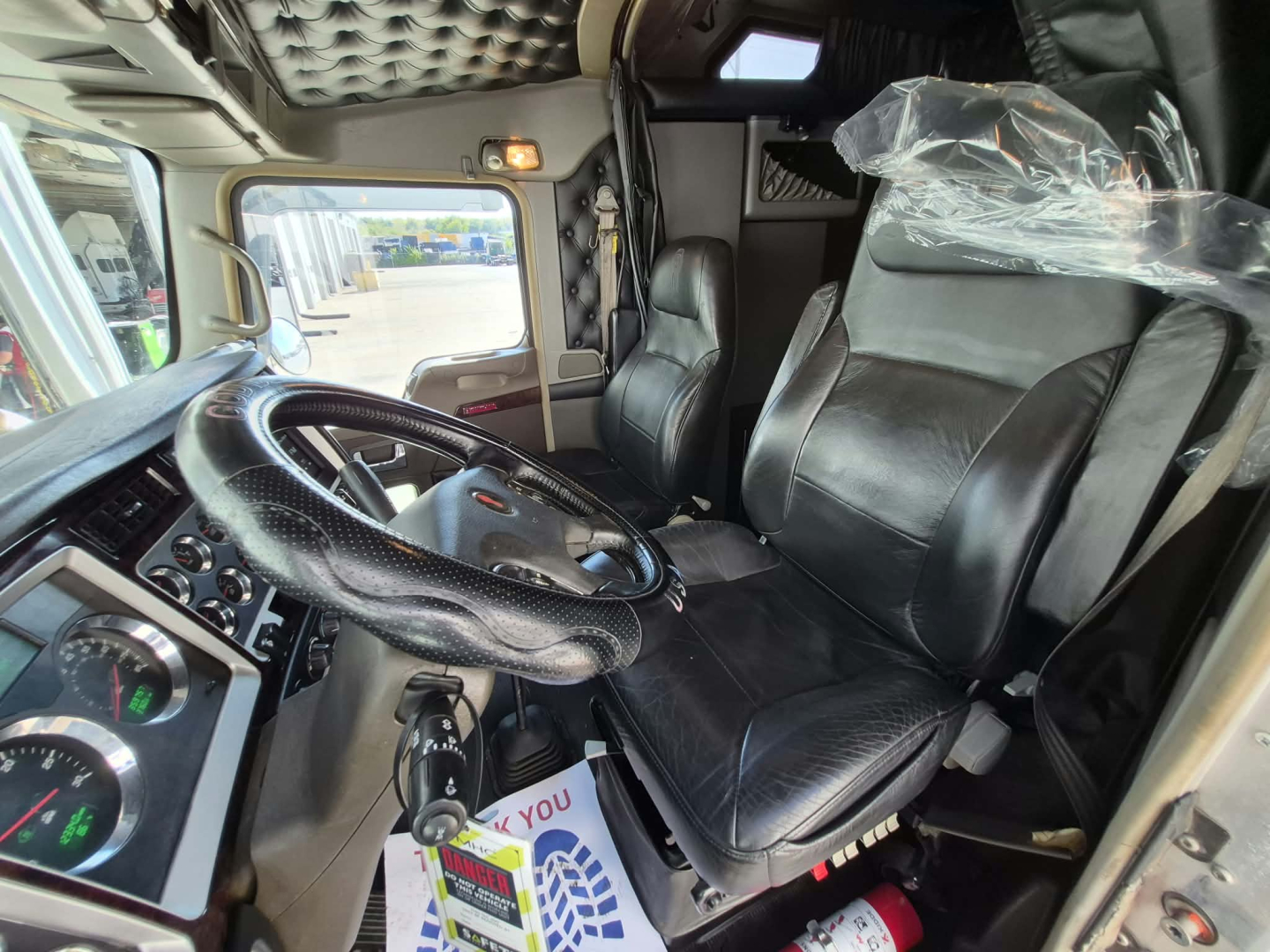 Kenworth W900L truck interior showing driver seat, steering wheel, and dashboard with quilted headliner.