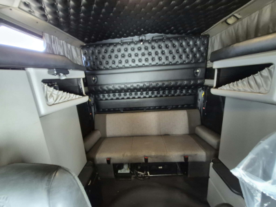 Kenworth W900L truck cab interior showing quilted black padded ceiling and walls, beige bunk seat, and overhead storage shelves.