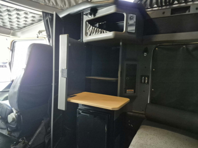 Kenworth W900L cab interior with a small wood table, storage shelves, and cab partition; driver seat visible and sleeper area in view.