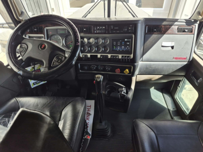Kenworth W900L truck interior showing steering wheel, dashboard with gauges, center console controls, and gear shifter.