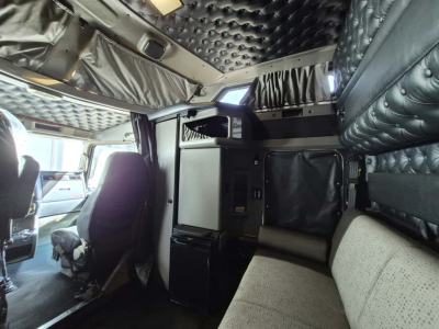 Kenworth W900L interior showing sleeper cab with quilted black padded ceiling, storage cabinet, small fridge, and seating area.