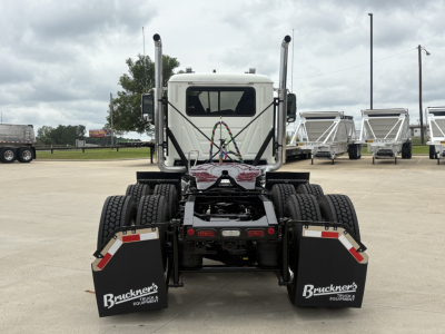 Tractor cab rear view of a new 2027 Mack PI64T sleeper/ daycab with dual rear axles and mud flaps, Bruckner trailer hitch branding visible on mud flaps.