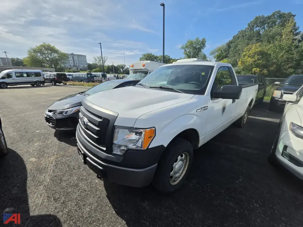 White 2012 Ford F-150 pickup truck in a used car lot, front-left view, with other vehicles nearby.