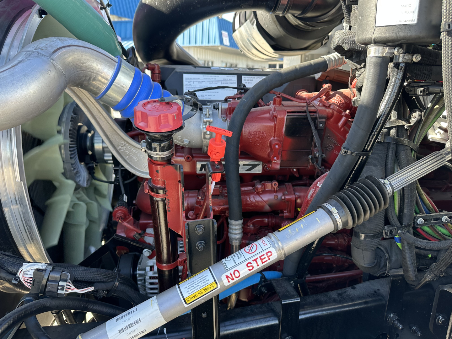 Mack GR64B engine bay showing red engine block, hoses, and orange/lred components with labels and a NO STEP decal on a cylindrical pipe.