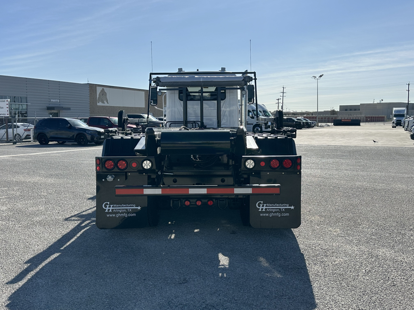 Rear view of a black Mack GR64B roll-off truck showing taillights, bumper, mud flaps with GEF sign, and rear hitch. Text on mud flaps includes 'www.ghfinc.com' and other branding.