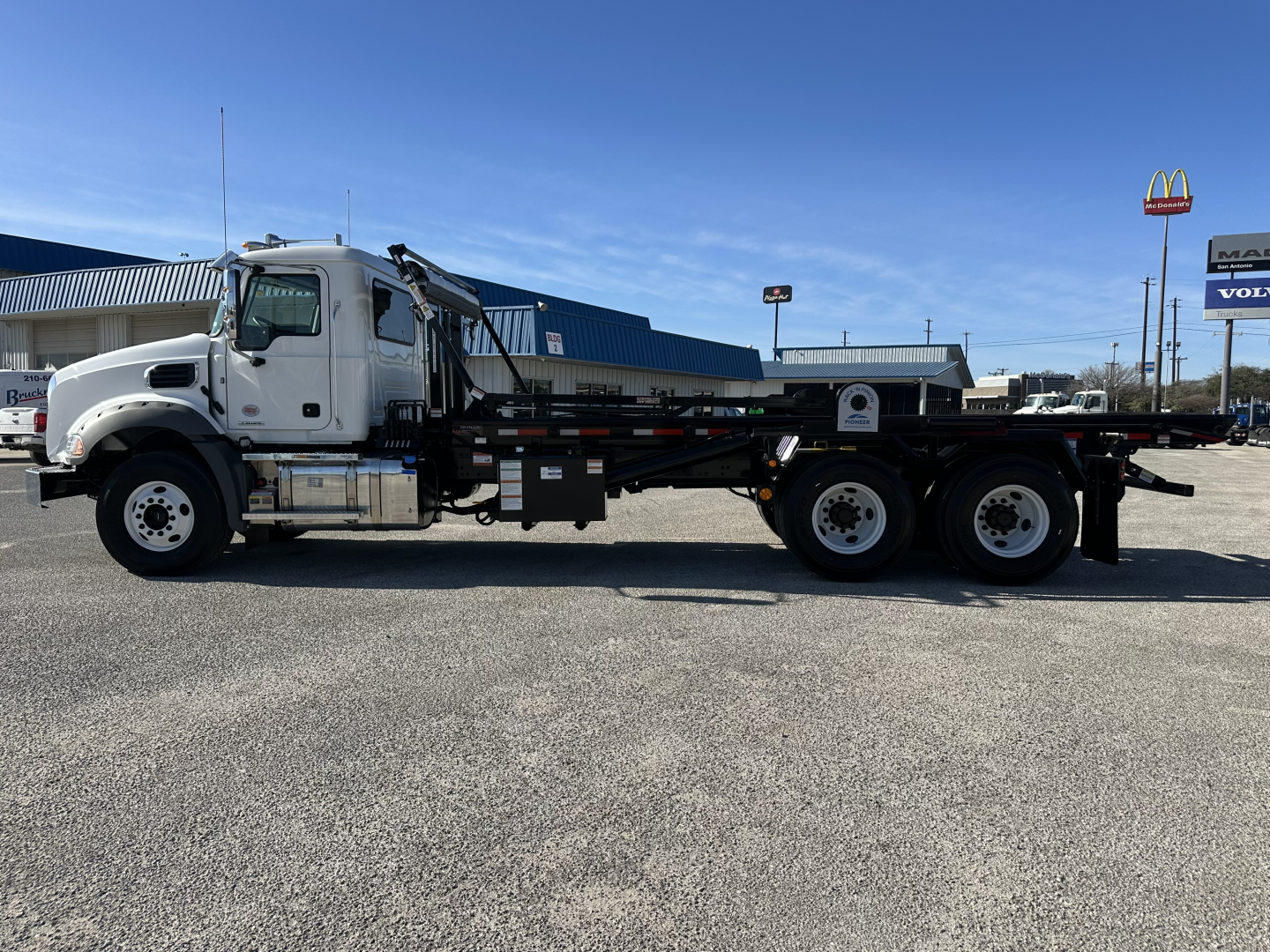 2026 Mack GR64B roll-off truck in side view with white cab, long black flatbed, and three rear axles.