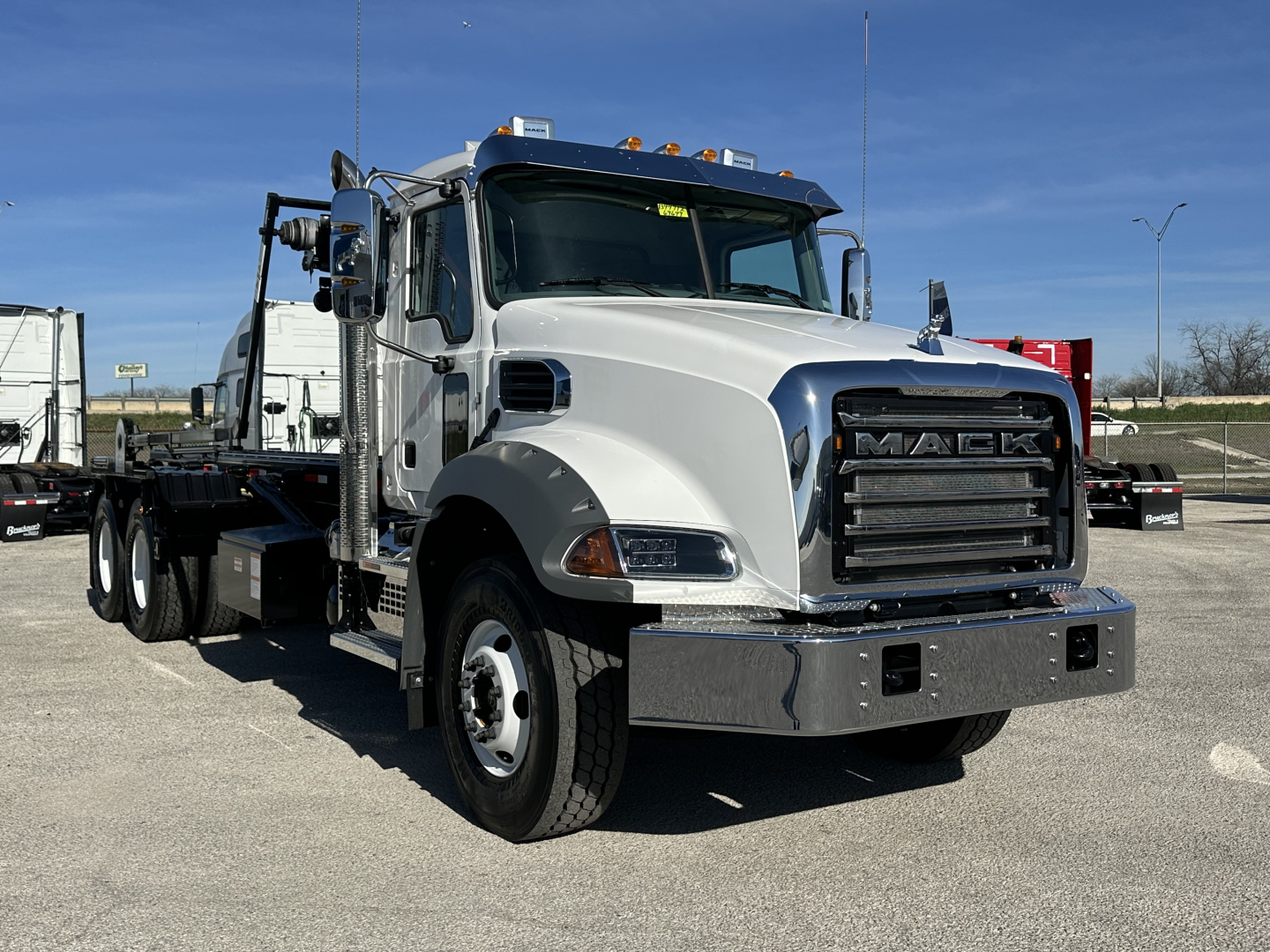 Mack GR64B roll-off truck in white and chrome showing front grille with Mack logo and heavy-duty bumper.