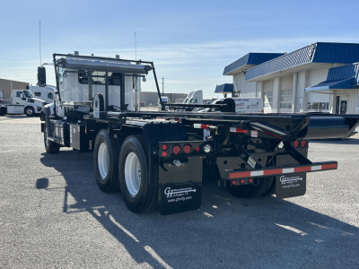 2026 Mack GR64B rolloff truck rear view showing flatbed/loader and dual rear axles with mud flaps
