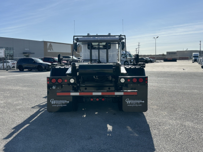 Rear view of a black Mack GR64B roll-off truck showing taillights, bumper, mud flaps with GEF sign, and rear hitch. Text on mud flaps includes 'www.ghfinc.com' and other branding.