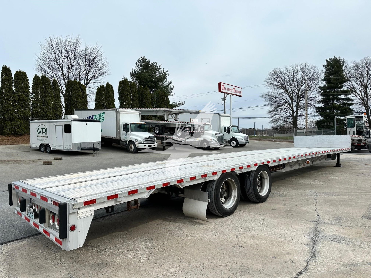 Drop deck trailer with extended flatbed showing dual rear axles and reflective safety markings.