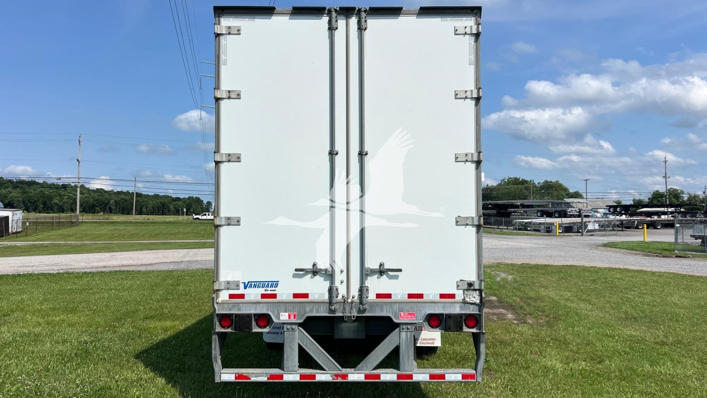 Rear view of a white Vanguard trailer with double doors and latching, red and white reflective tape, and bumper supports.