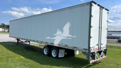 Trailer side view showing long gray Vanguard Vip Sheet & Post trailer with dual rear doors and white birds graphic on side.