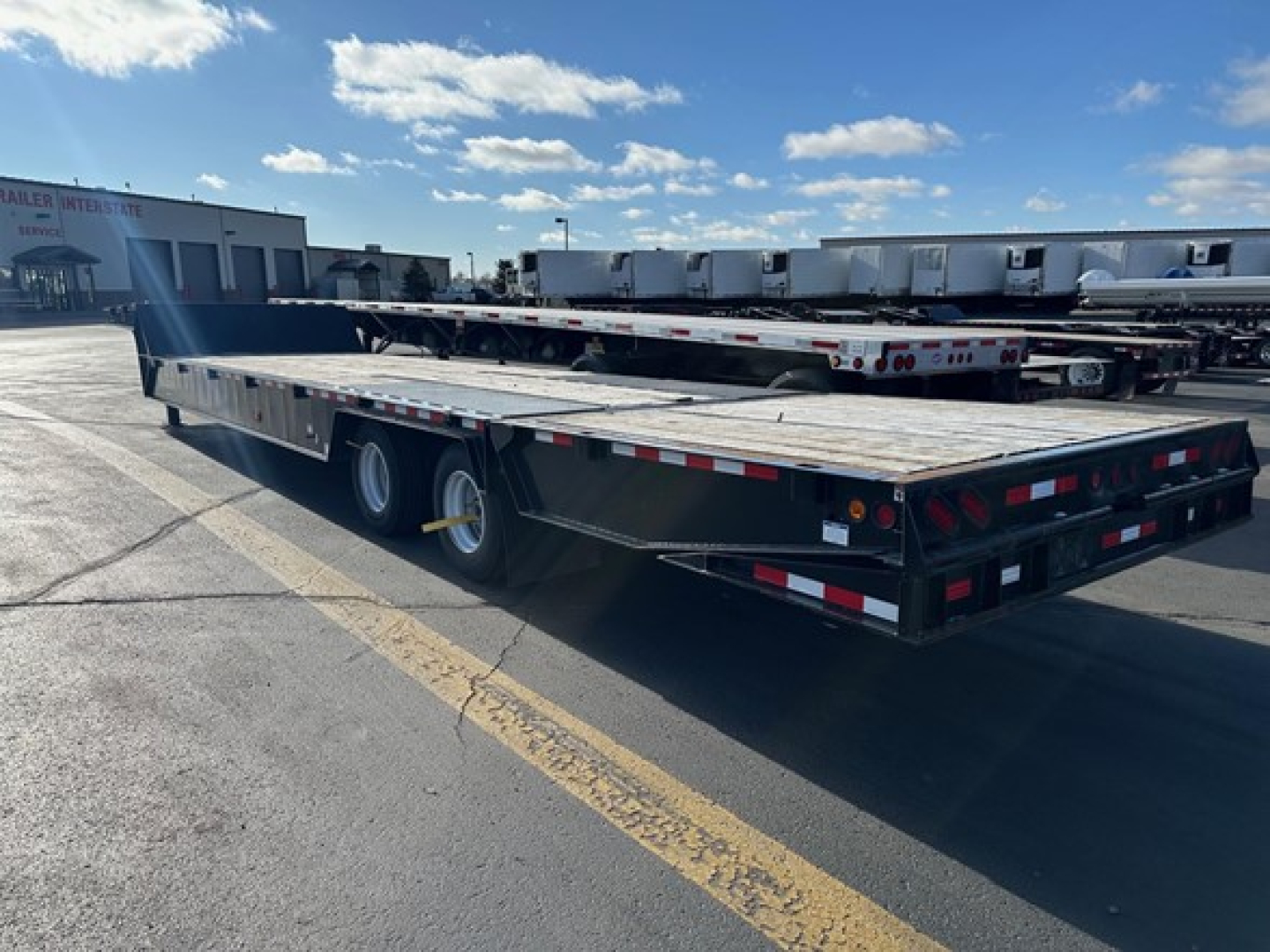 Trailer showing 7-axle trailer with flatbed and dual rear wheels, black frame, red/white safety markings, and open wooden deck.