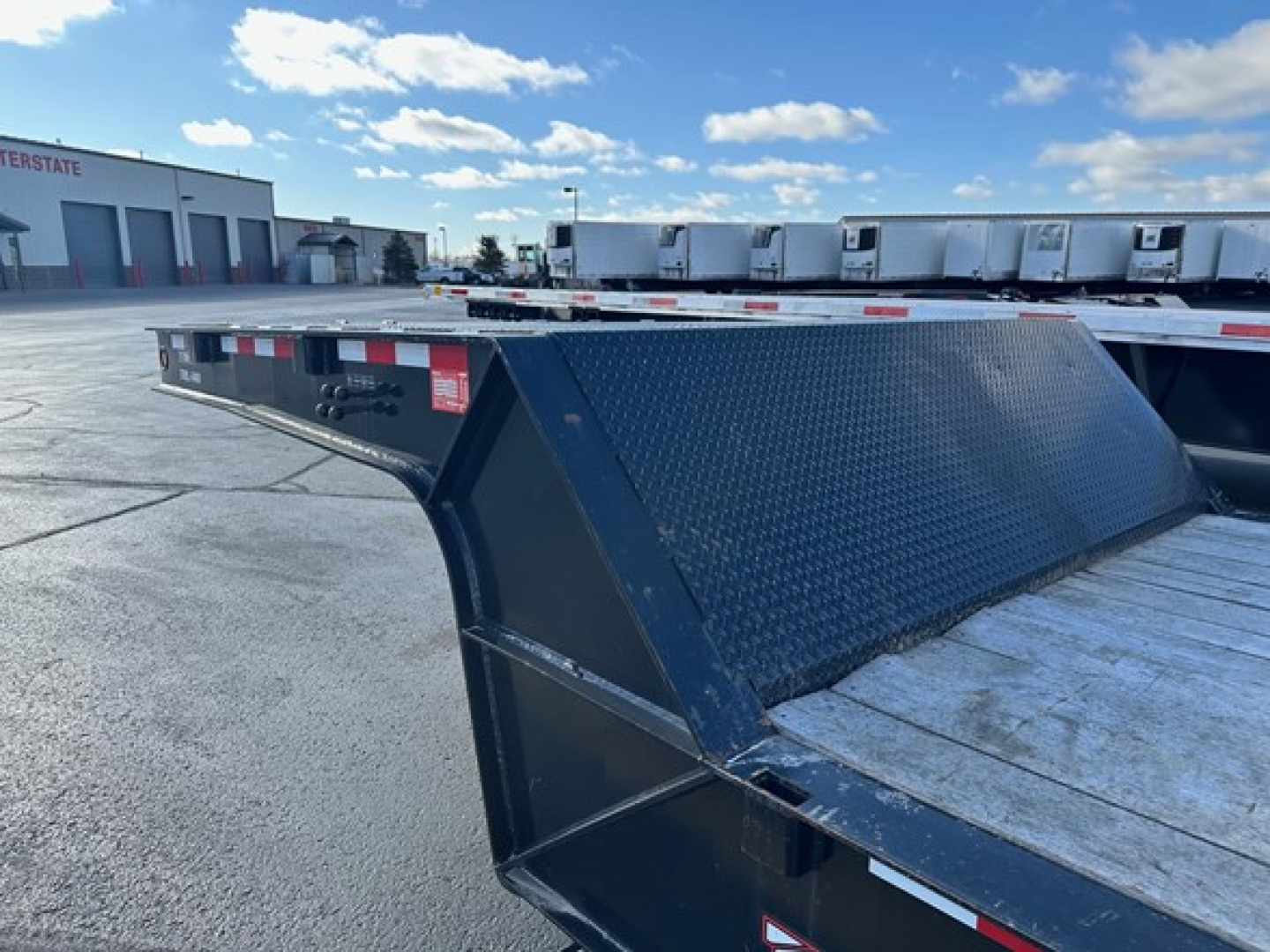 Trailer deck with a reinforced steel ramp and diamond-plate surface, blue paint, side rails, and utility markings on a truck yard.