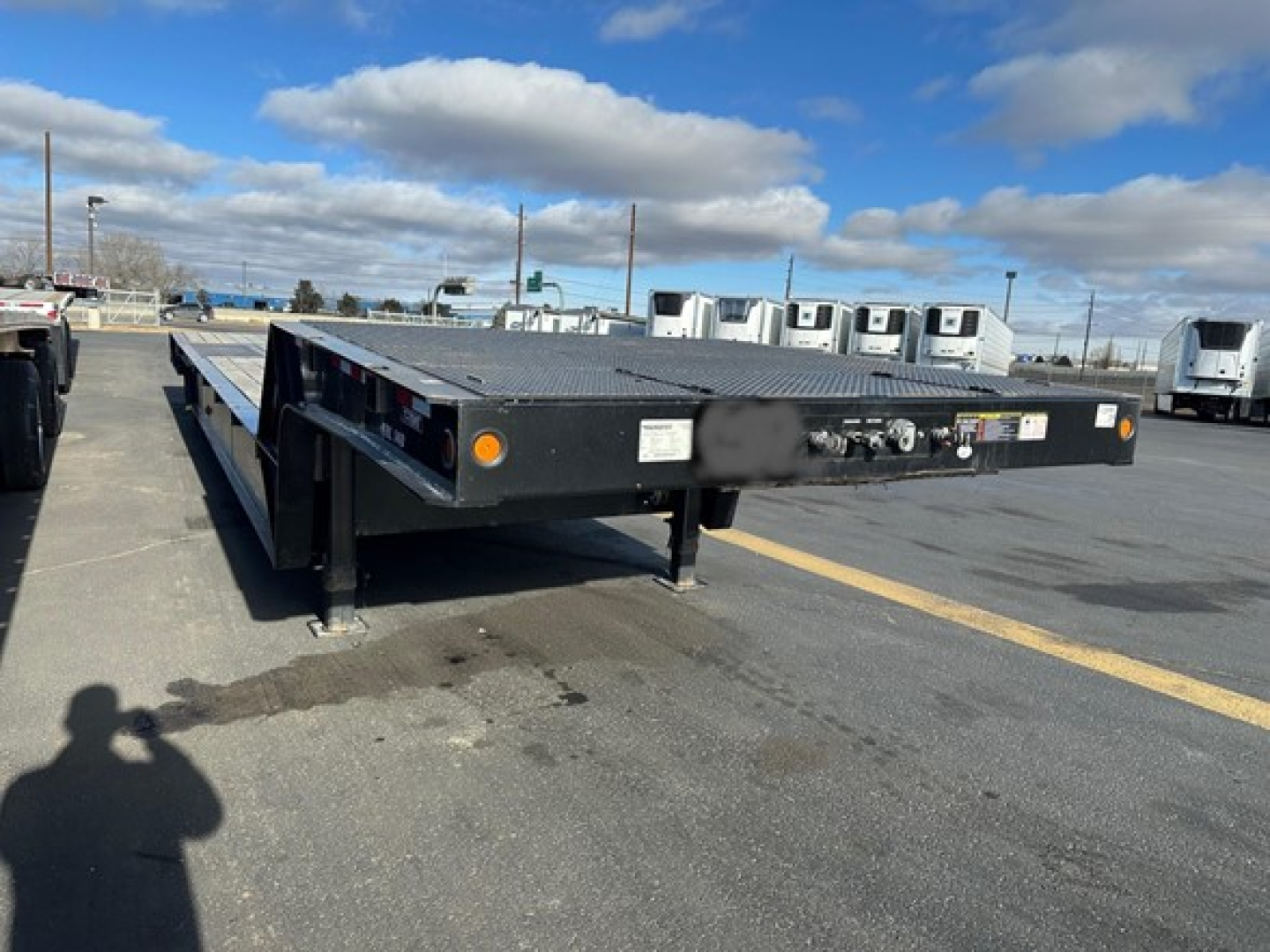 Trailking 7-70Ht trailer flatbed in a lot, low-angle view showing side deck and loading ramps with some tires and equipment in background.