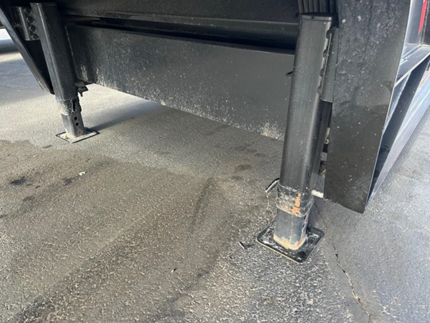 Trailking trailer leg with adjustable jack stands on a paved surface; dirt and grime visible on the legs and ground.