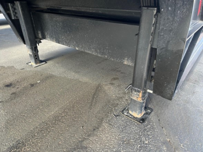 Trailer landing gear and undercarriage stabilizer leg showing square base plate and hydraulic support with dirt/grime on concrete surface.
