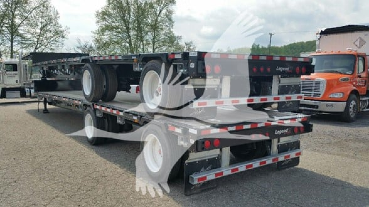Manac drop deck trailer in a yard showing dual axle with wheels and flatbed sections.