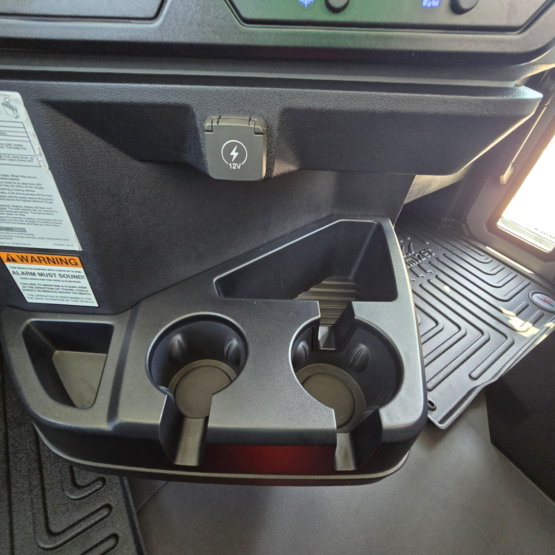Cab interior of a 2027 Mack GR64B mixer truck showing cup holders, a 12V power outlet cover, and storage compartments.