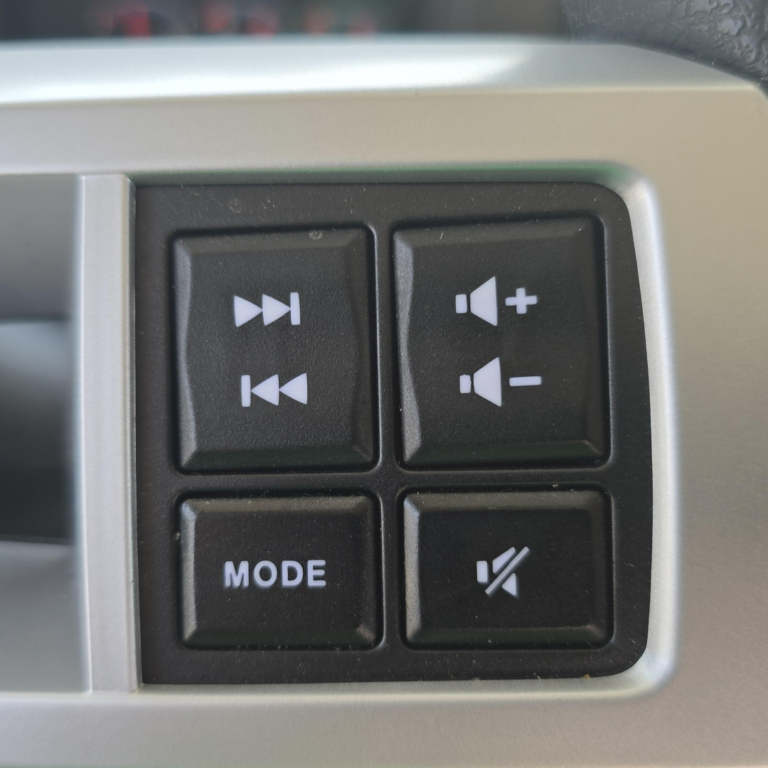 Cockpit control switches on Mack GR64B mixer showing mode button and volume controls with icons for media and mute.