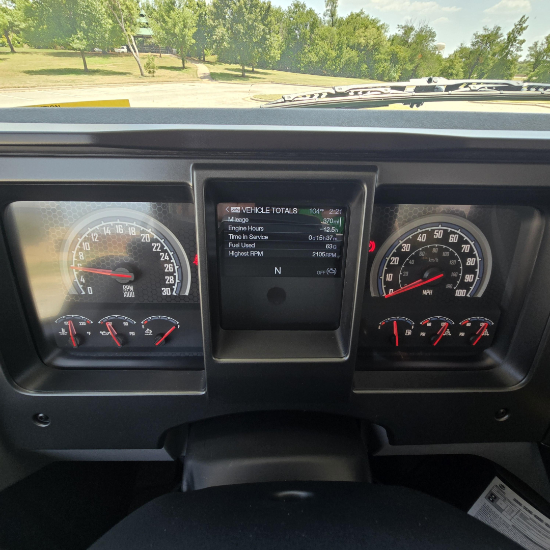 Dashboard of a Mack GR64B showing instrument cluster with miles, engine hours, fuel, and RPM; center display lists vehicle totals.