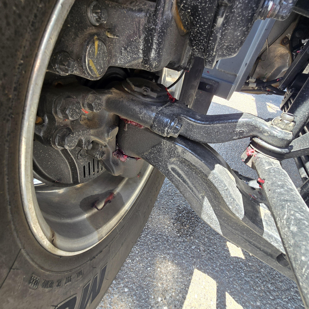 Mack GR64B front suspension and wheel area showing hydraulic lines and steering linkage.