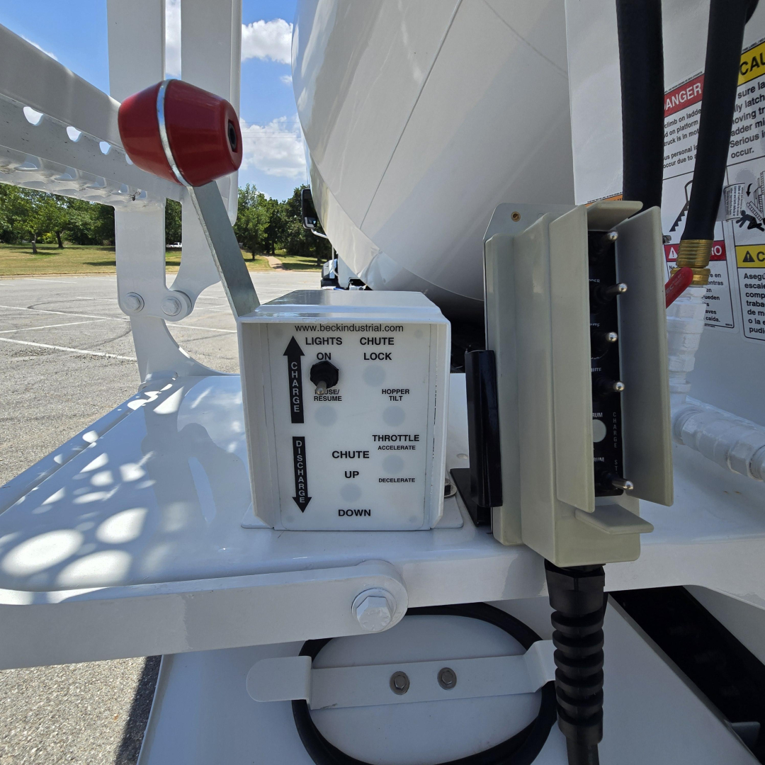 Mixer truck hitch area showing control box and lever with labels: BECK INDUSTRIAL lights on/off arrow, choke, up, down; adjacent hydraulic controller and hydraulic hose reel.