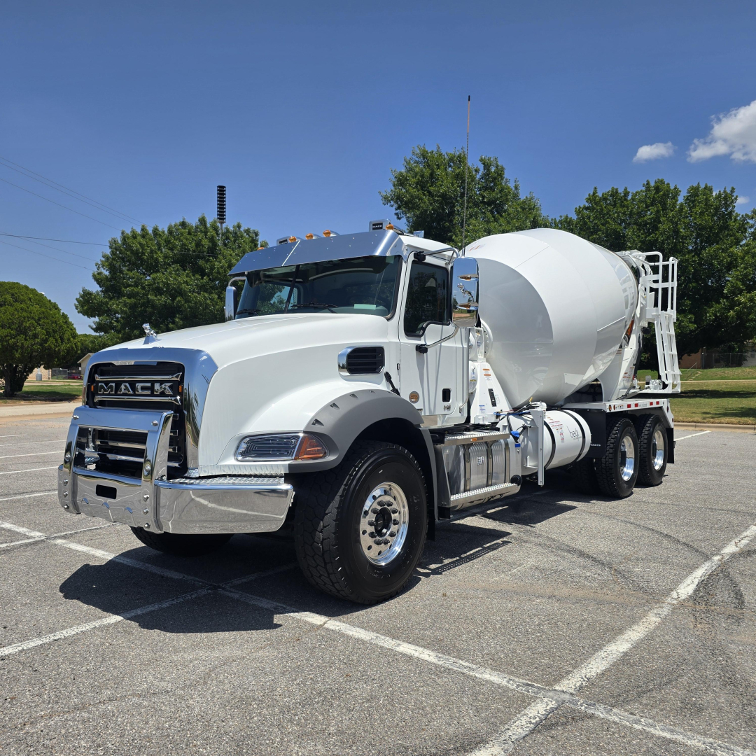 Mack GR64B mixer truck in a parking lot, white cab and cement mixer on long chassis with chrome accents.