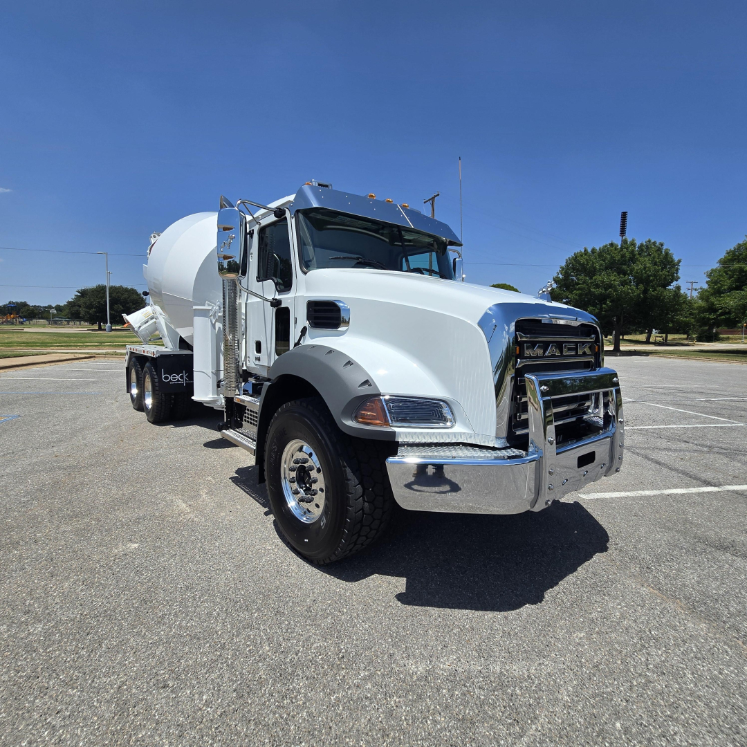 Mack GR64B mixer truck in a parking lot, white with chrome grille, front view showing mixer drum and side mirrors.