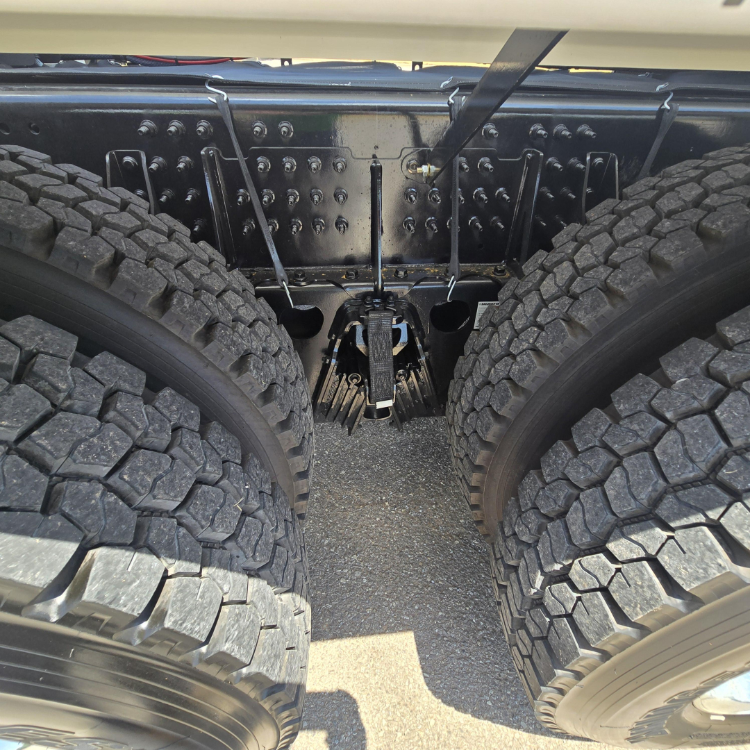 Rear view of 2027 Mack GR64B mixer chassis showing dual rear axles and drivetrain clearances, with heavy-duty suspension and metal frame components visible.