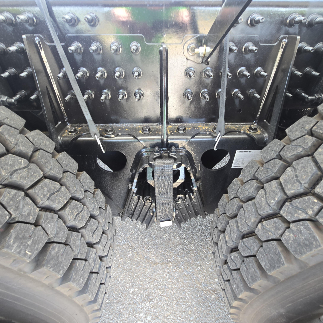 Mack GR64B chassis rear view showing heavy dual tires and hitch assembly with numerous bolts and a gear-like mechanism at center.