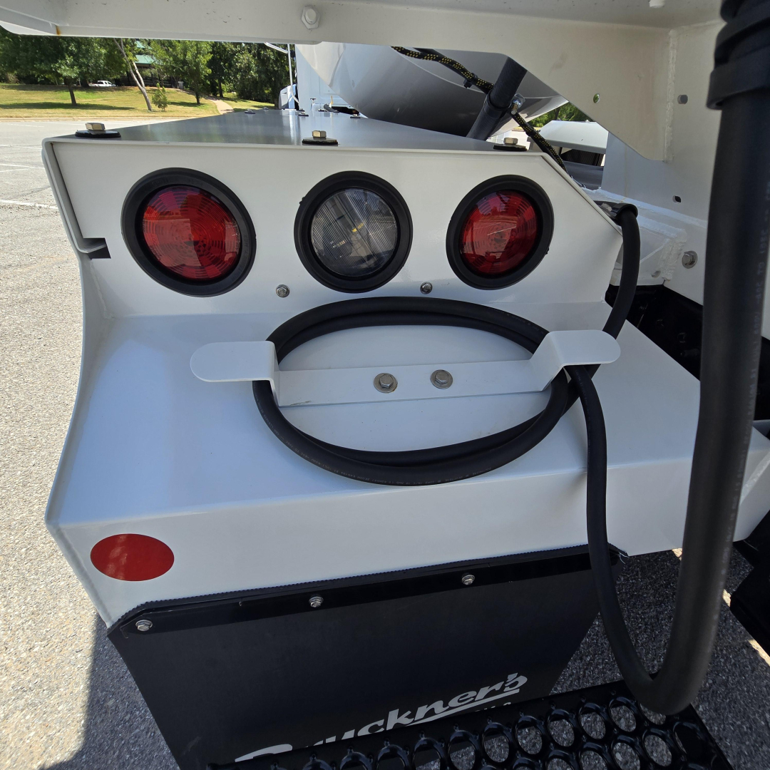 Back view of a white Mack mixer truck showing three circular rear lights and a coiled hose storage mount on the tailgate area.