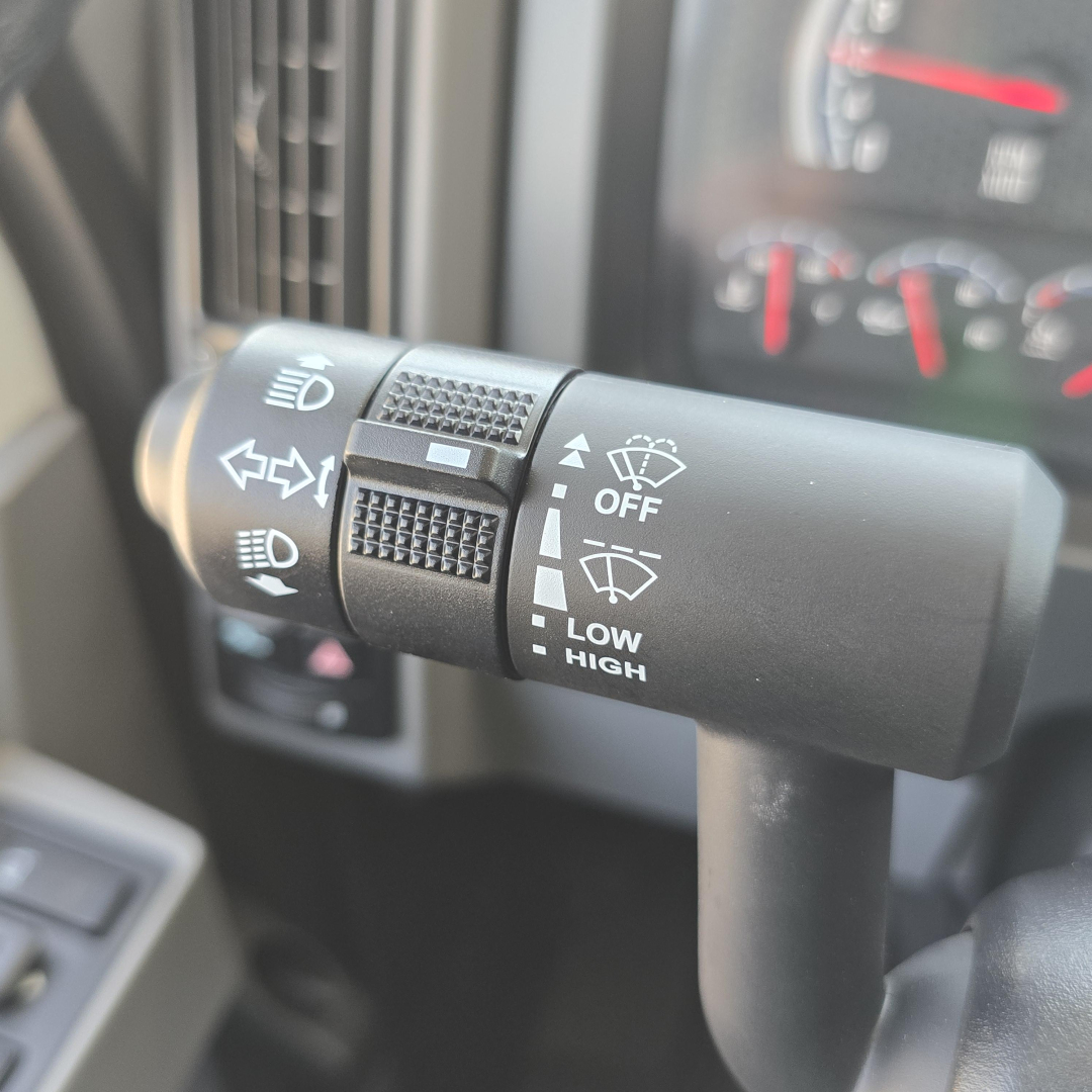 Truck steering column stalk with headlight and wiper controls in view, Mack GR64B, gauge cluster blurred in background