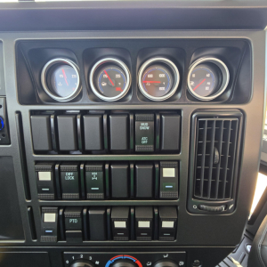 Dashboard gauges and switches of a 2027 Mack GR64B mixer truck showing multiple analog gauges and control switches.