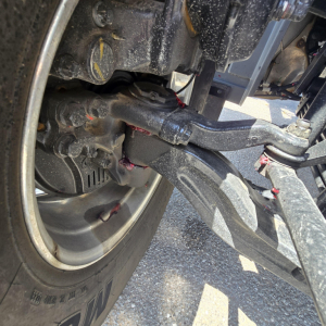 Mack GR64B front suspension and wheel area showing hydraulic lines and steering linkage.