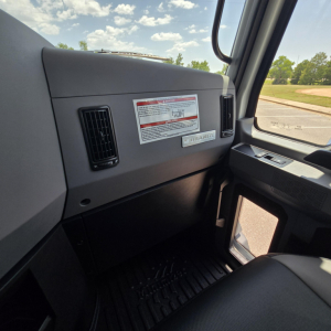 Truck interior showing dashboard and passenger side window of a 2027 Mack GR64B mixer truck. Visible label on the dash and air vent with light entering from outside.