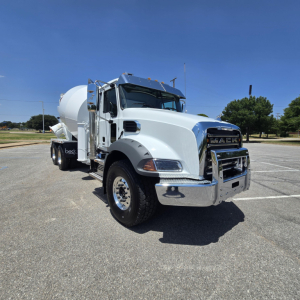 Mack GR64B mixer truck in a parking lot, white with chrome grille, front view showing mixer drum and side mirrors.