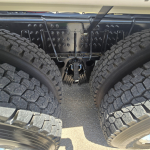 Rear view of 2027 Mack GR64B mixer chassis showing dual rear axles and drivetrain clearances, with heavy-duty suspension and metal frame components visible.