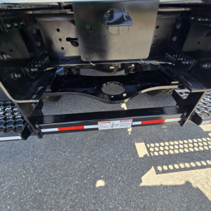 Rear view of a 2027 Mack GR64B mixer truck showing hitch area and underside components with a reflective red-and-white safety strip.