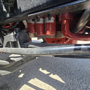 Underbody of a Mack mixer truck showing red coolant/filters and hydraulic lines with black frame and red pipes.