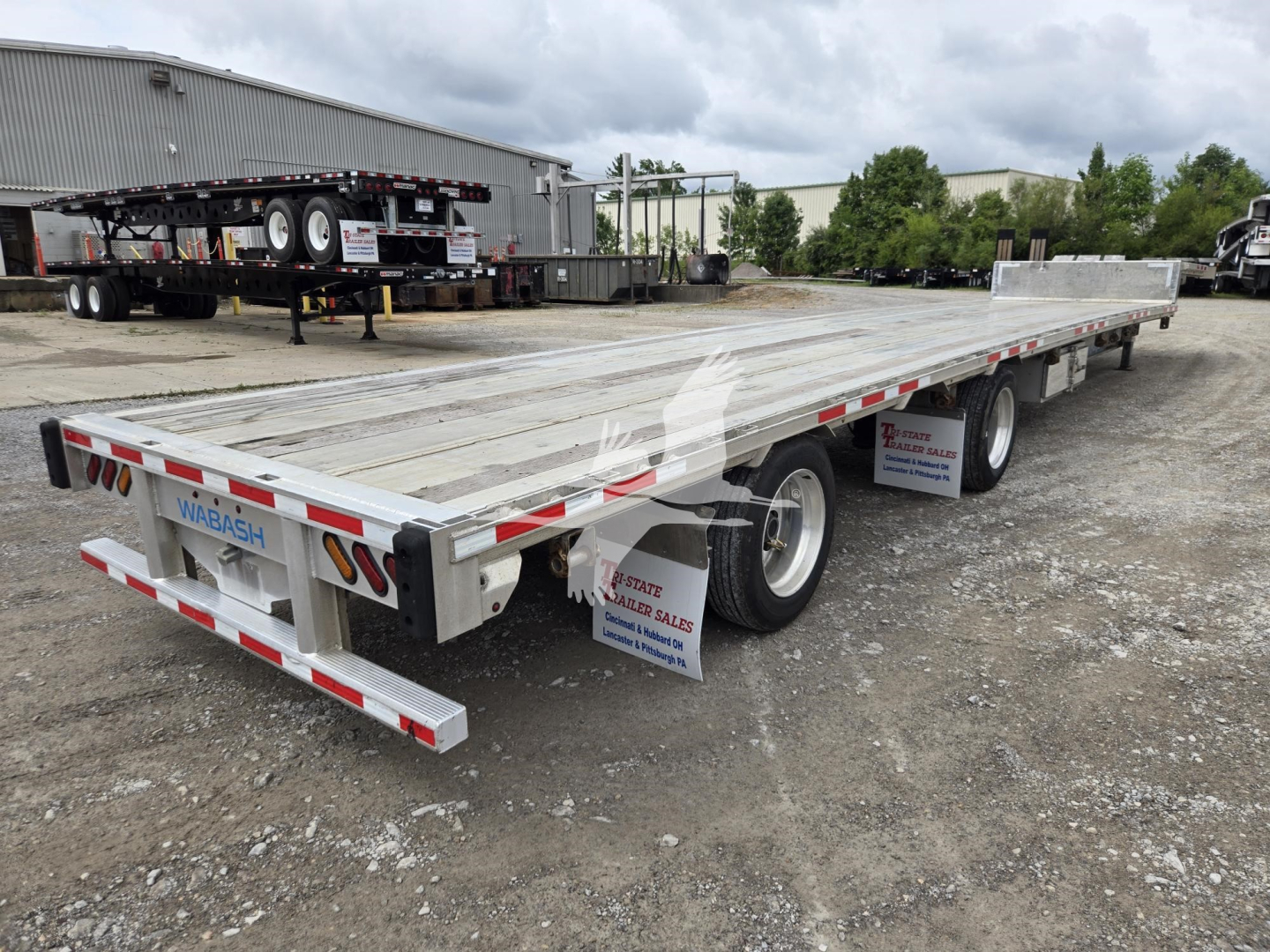 Wabash aluminum drop deck trailer showing long flatbed with wheels along the sides and rear; white and red reflective tape; VIN plate and stock number visible.