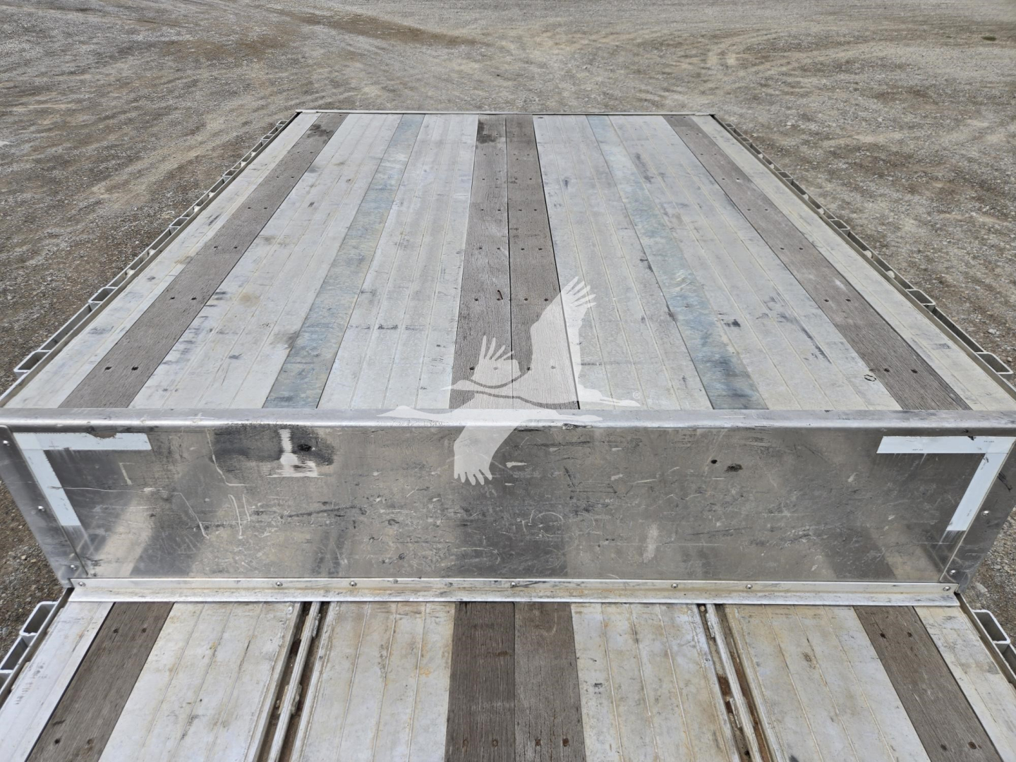 Aluminum drop deck trailer bed showing silver planks with wooden center strips and reinforced side rails.