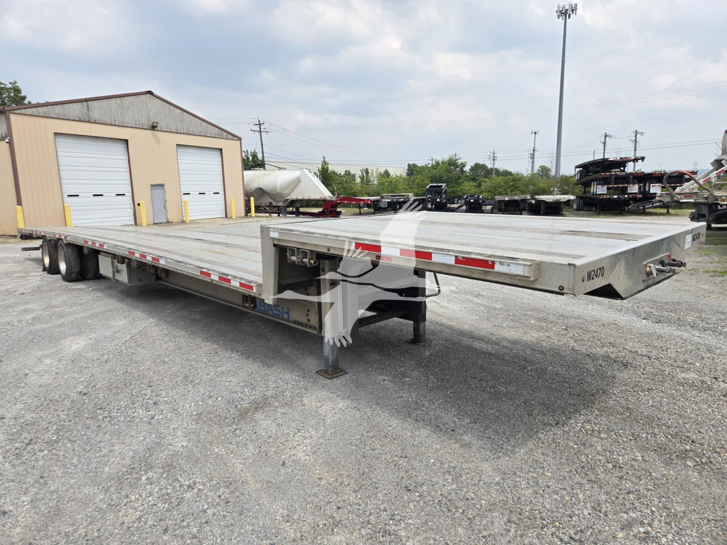 Trailer deck showing a Wabash drop deck trailer with aluminum flatbed, side rails, and landing gear; visible markings include reflective red/white tape along the sides and a slightly raised neck at the front.