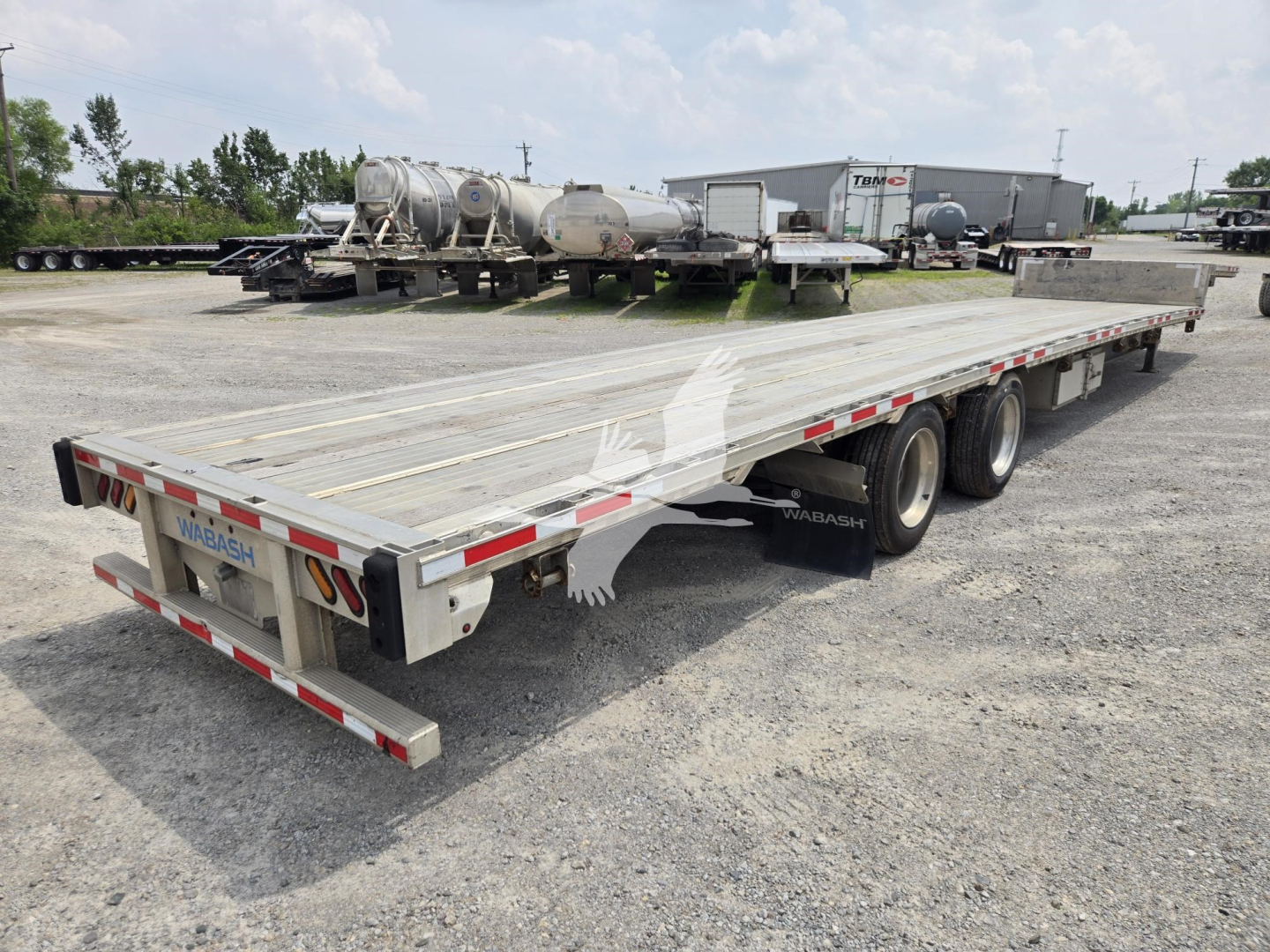Long Wabash drop deck trailer showing aluminum flatbed with triple-axle rear and rear bumper, reflective tape, and 'WABASH' branding at tail.