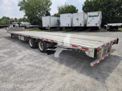 Trailer showing a long flatbed drop deck with three axles and dual tires; background includes several white refrigerated trailers and trees. Visible text includes 'Baylor' on one of the trailers and reflective safety markings on the sides.