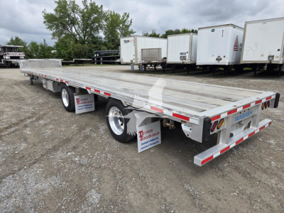 Aluminum drop deck trailer in an outdoor lot, long flatbed with dual rear axles and red/white reflective tape, WABASH branding on rear, trailer legs visible.
