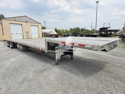 Trailer deck showing a Wabash drop deck trailer with aluminum flatbed, side rails, and landing gear; visible markings include reflective red/white tape along the sides and a slightly raised neck at the front.