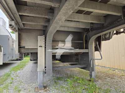 Trailer undercarriage showing drop deck trailer frame and suspension with adjustable legs and support beams.